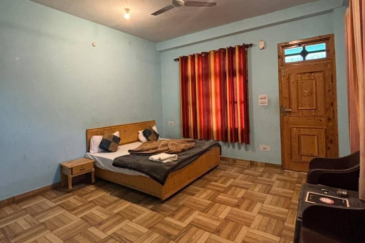 Una habitación con una cama, un ventilador de techo, una puerta de madera y una mesita.