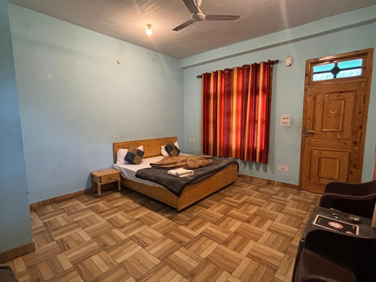 A bedroom with a bed, a nightstand, a desk, a ceiling fan, and a door.