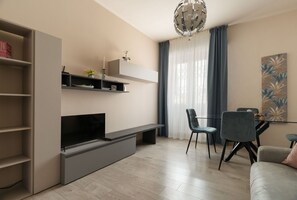 Un salon moderne doté d’un téléviseur à écran plat, d’étagères intégrées, d’un coin repas avec des chaises et d’un lustre.