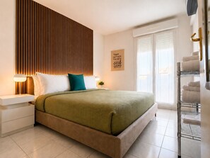 A modern bedroom with a bed, bedside tables, a wall-mounted light, a window with blinds, and a towel rack. - La Terrasse Bleue-Private covered parking 150 m from Juan Les Pins beach (Antibes)