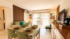 A modern kitchen with a dining table set for four, a sofa, a TV, and a sliding glass door leading to an outdoor area. - La Terrasse Bleue-Private covered parking 150 m from Juan Les Pins beach (Antibes)