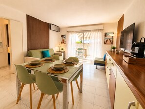 A modern kitchen with a dining table set for four, a sofa, a TV, and a sliding glass door leading to an outdoor area. - La Terrasse Bleue-Private covered parking 150 m from Juan Les Pins beach (Antibes)