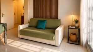 A modern living room with a sofa, a side table with a lamp, and a wall-mounted air conditioner. - La Terrasse Bleue-Private covered parking 150 m from Juan Les Pins beach (Antibes)