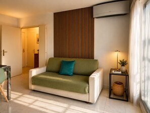 A modern living room with a sofa, a side table with a lamp, and a wall-mounted air conditioner. - La Terrasse Bleue-Private covered parking 150 m from Juan Les Pins beach (Antibes)