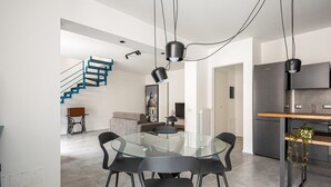 Una cocina moderna con refrigerador empotrado, un comedor con mesa y sillas de vidrio, y una escalera con barandillas azules.