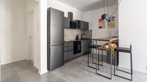 Una cocina moderna con refrigerador, horno y microondas. Hay una mesa de comedor con sillas y una lámpara colgante.