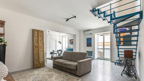 Una sala de estar con un sofá, un tapete estampado, una máquina de coser antigua y una escalera espiral azul.