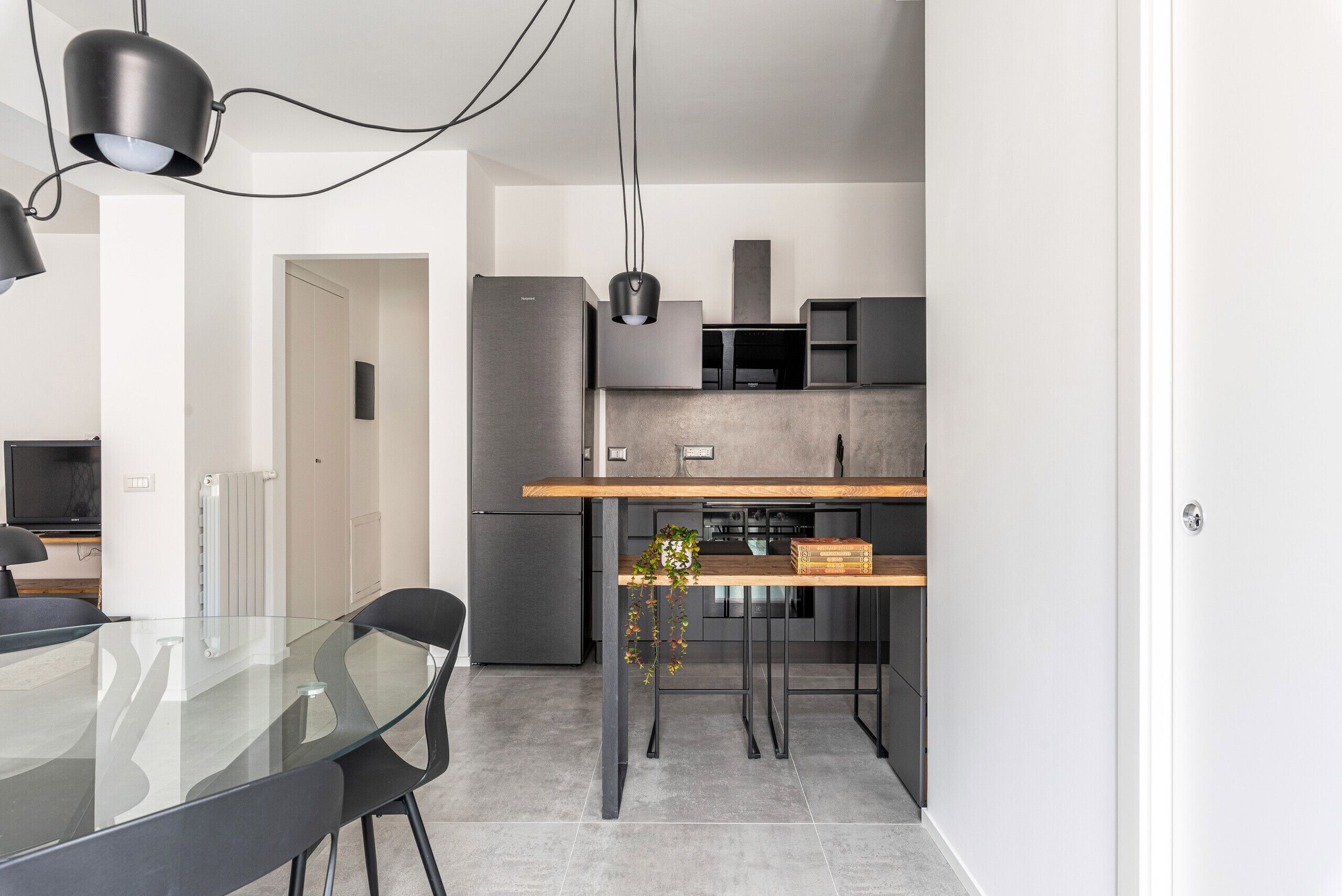A modern kitchen with a glass dining table, black chairs, and pendant lighting.