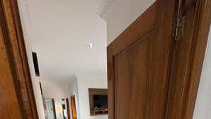 Un pasillo con puerta de madera, suelo de baldosas y un televisor montado en la pared.