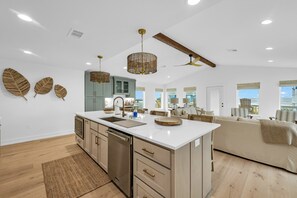 Eine moderne Küche mit einer zentralen Kochinsel, Wanddekoration aus Holzblättern und einem Deckenventilator.