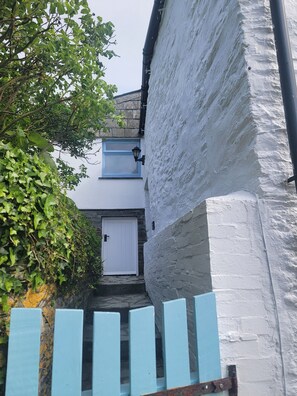Une ruelle étroite avec un bâtiment blanc, une porte bleue et une petite fenêtre.