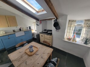 Una cocina con tragaluz, armarios de madera, una mesa de comedor con una bandeja y una ventana con cortinas.