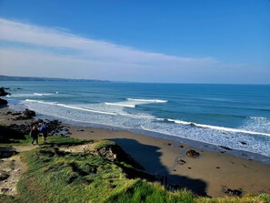 Un paisaje costero con una playa arenosa, afloramientos rocosos y un cielo azul despejado.