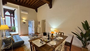 A dining area with a wooden table set for four, surrounded by white chairs, a sofa, and a lamp. - Cosy apartment for 8 guests with WIFI, A/C, TV and balcony (Lucca)
