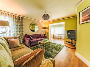 Ein Wohnzimmer mit einer Couch, einem Couchtisch, einem Fernseher und einem runden Spiegel an der Wand.