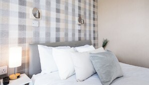 Un letto rifatto con cuscini bianchi e grigi, una lampada da comodino e un telecomando su un comodino bianco.