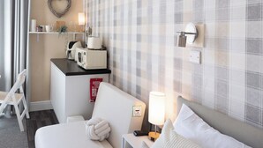 Habitación de hotel con pared a cuadros, una cama, una mesita de noche con lámpara, un microondas y un cartel de manta ignífuga.