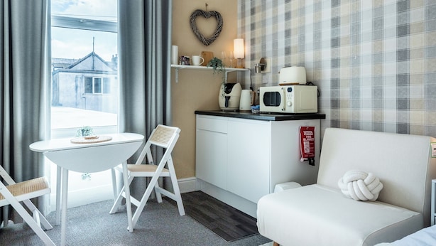 Una habitación con una mesa de comedor, una silla blanca, un sofá, un microondas, una pequeña encimera de cocina y una decoración con forma de corazón en la pared.