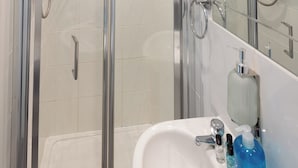 Un baño moderno con ducha envuelta en cristal, un lavabo blanco con artículos de aseo y un espejo que refleja el ambiente.