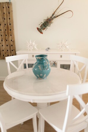 Une table ronde blanche, ornée d’un vase turquoise au centre, et entourée de chaises blanches.
