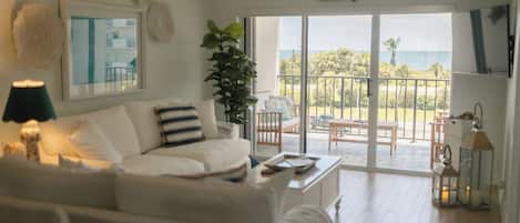 A modern living room with a white sofa, a coffee table, and a large window offering a view of the outdoors.