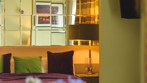 Quarto de hotel com cama, almofadas, mesa de cabeceira, abajur e janela com cortinas.