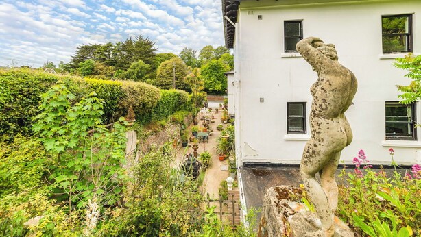 Um edifício branco com uma escultura de pedra, vegetação exuberante e um céu claro.