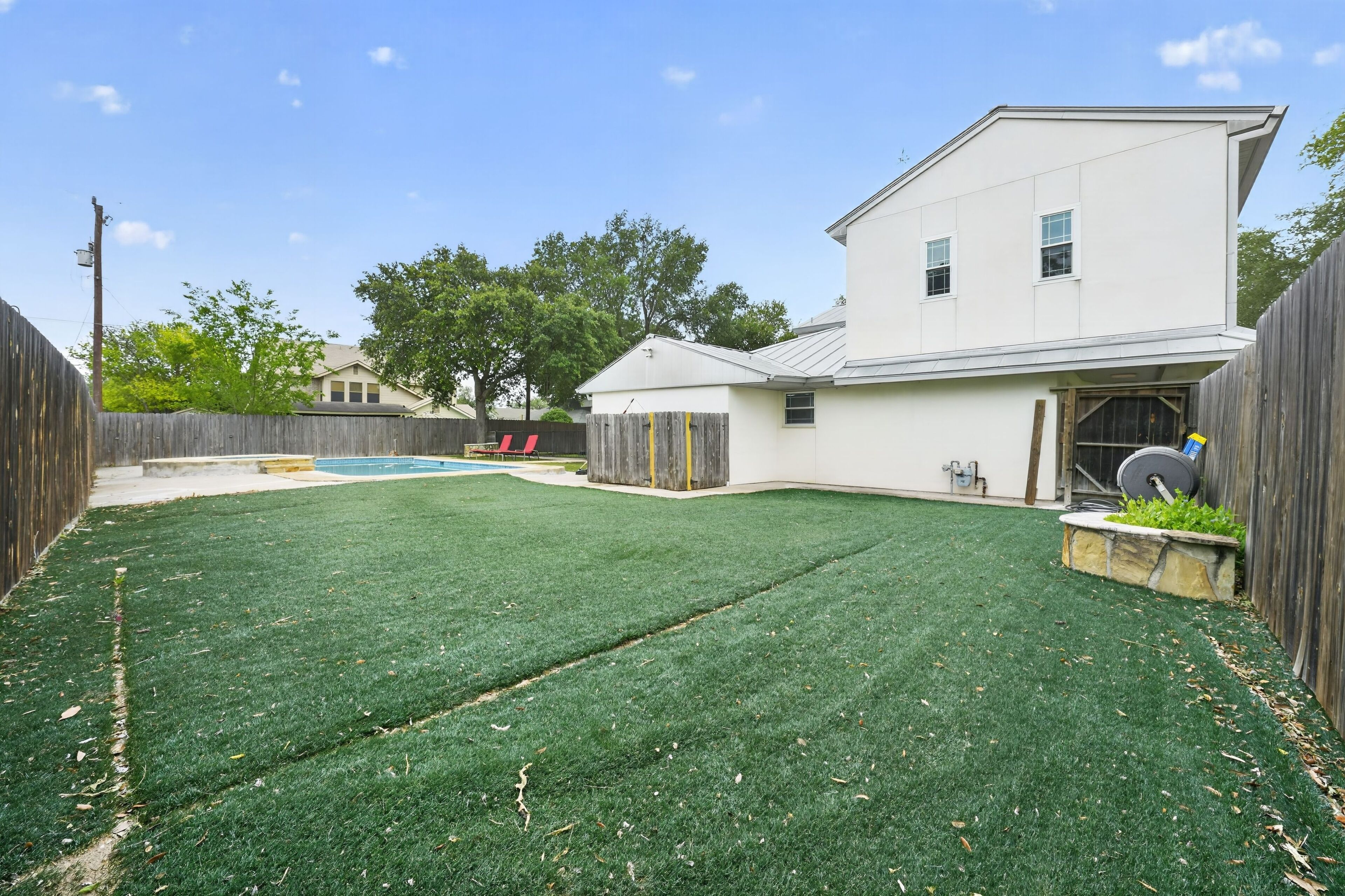 A backyard with artificial grass, a wooden fence, and a building with a garage.