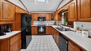 A kitchen with wooden cabinets, a black refrigerator, a microwave, and a sink. - Unadilla Riverfront Oasis 3br Sleeps 8 3 Bedroom Home (Unadilla)