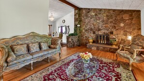 A room with a stone wall, a wooden ceiling, a sofa, a chair, a glass coffee table, and a rug. - Unadilla Riverfront Oasis 3br Sleeps 8 3 Bedroom Home (Unadilla)