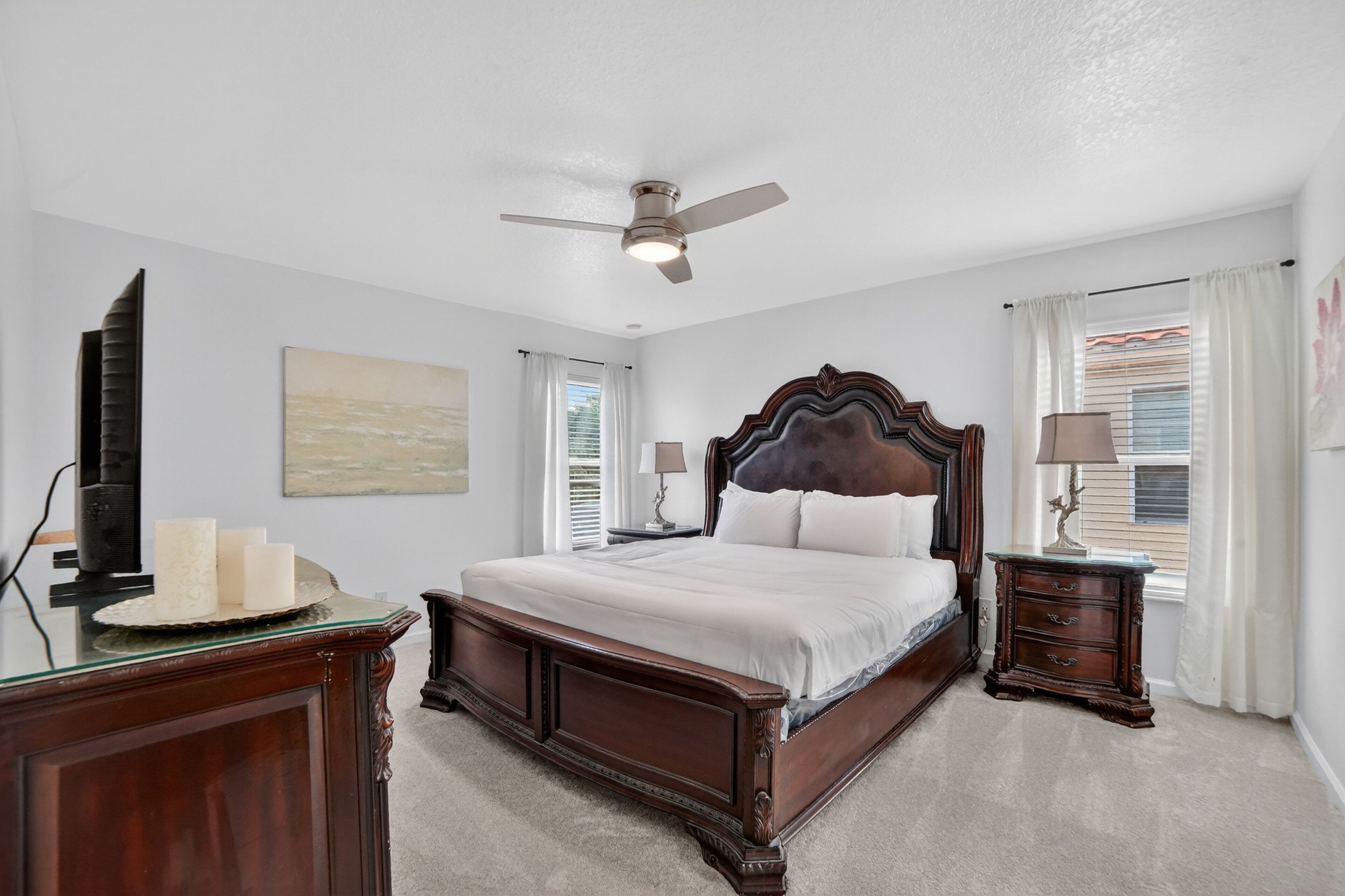 A bedroom with a wooden bed, a ceiling fan, a nightstand, a lamp, and a window with curtains.