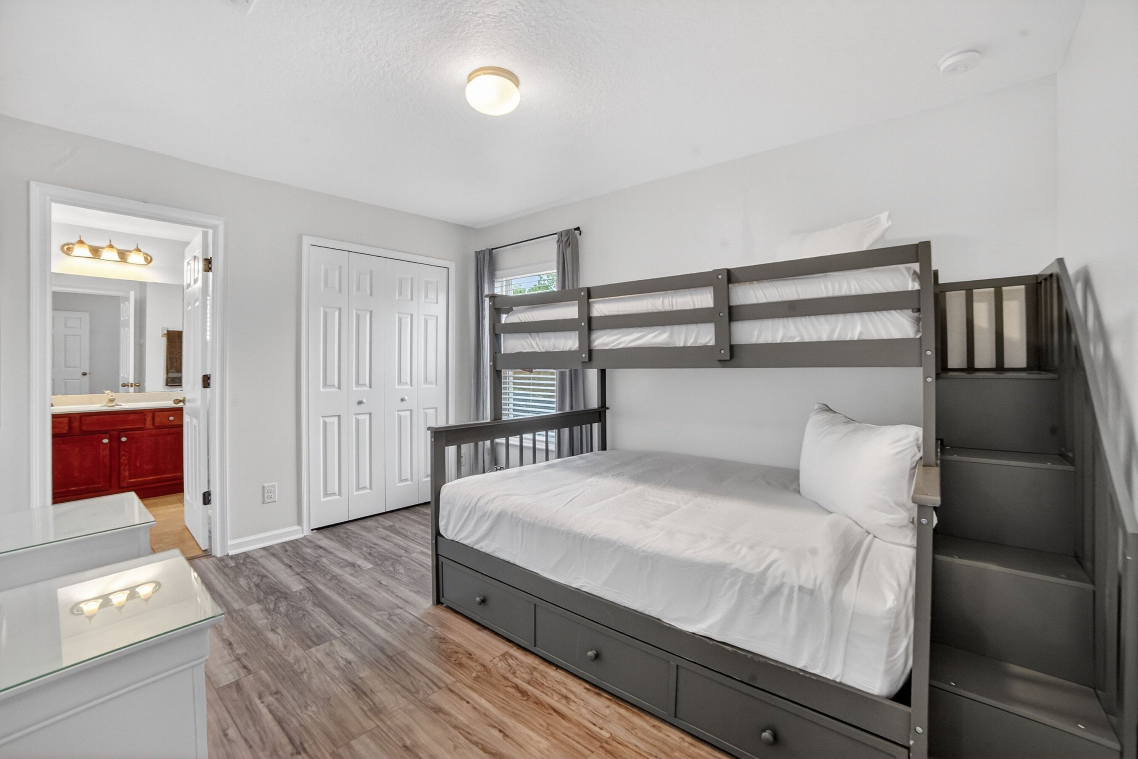 A bedroom with a bunk bed, a dresser, a mirror, and a door leading to a bathroom.