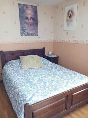 Une chambre à coucher avec un lit, une table de chevet, une lampe fixée au mur et deux affiches.