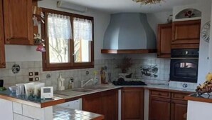 Una cucina con mobili in legno, forno incassato e finestra con tenda.