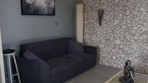 Un soggiorno con un divano dai toni scuri, un tavolino da caffè in vetro, un quadro appeso e una parete con decorazione effetto pietra.