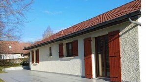 Una casa a un piano con tetto in tegole rosse, pareti esterne bianche e vialetto in cemento.