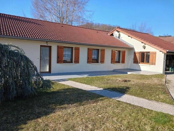 Un bâtiment à deux étages, doté d’un toit recouvert de tuiles rouges, d’un patio abrité et d’une cour gazonnée.