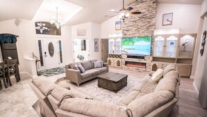 Ein geräumiges Wohnzimmer mit einer großen Eckcouch, einem Kamin, einem Flachbildfernseher und einem Essbereich mit einer Pendelleuchte.