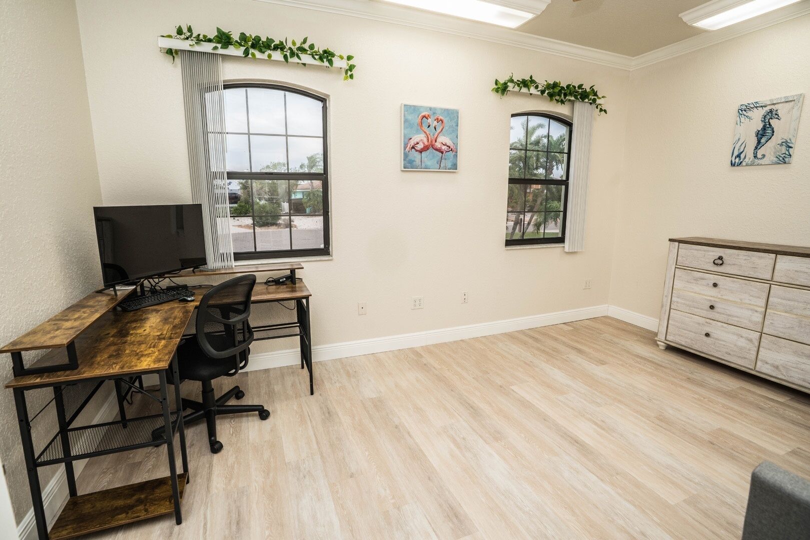Una habitación con escritorio, silla, computadora, dos ventanas y cómoda.