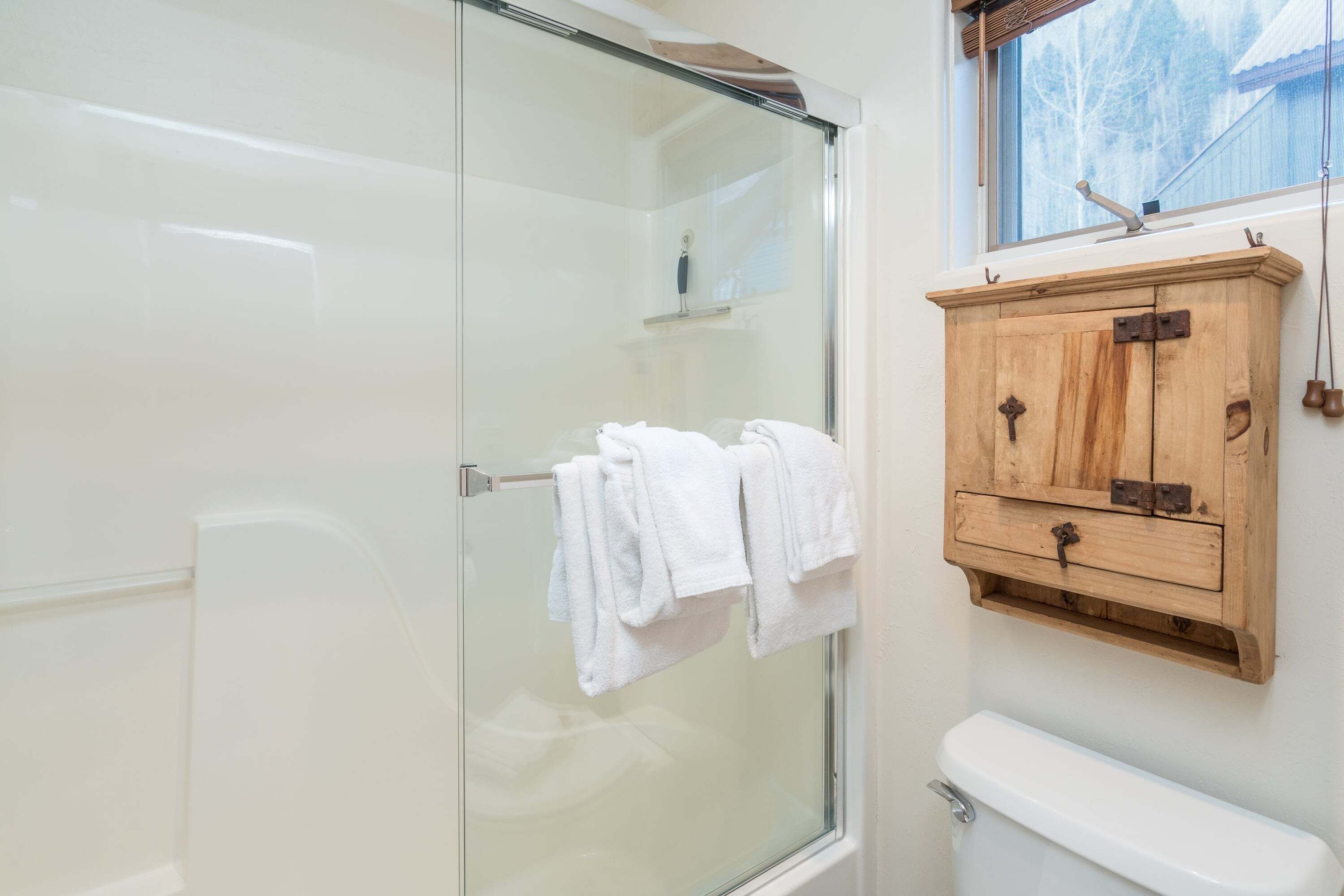 A bathroom with a glass shower enclosure, a wooden cabinet with towels, and a toilet.