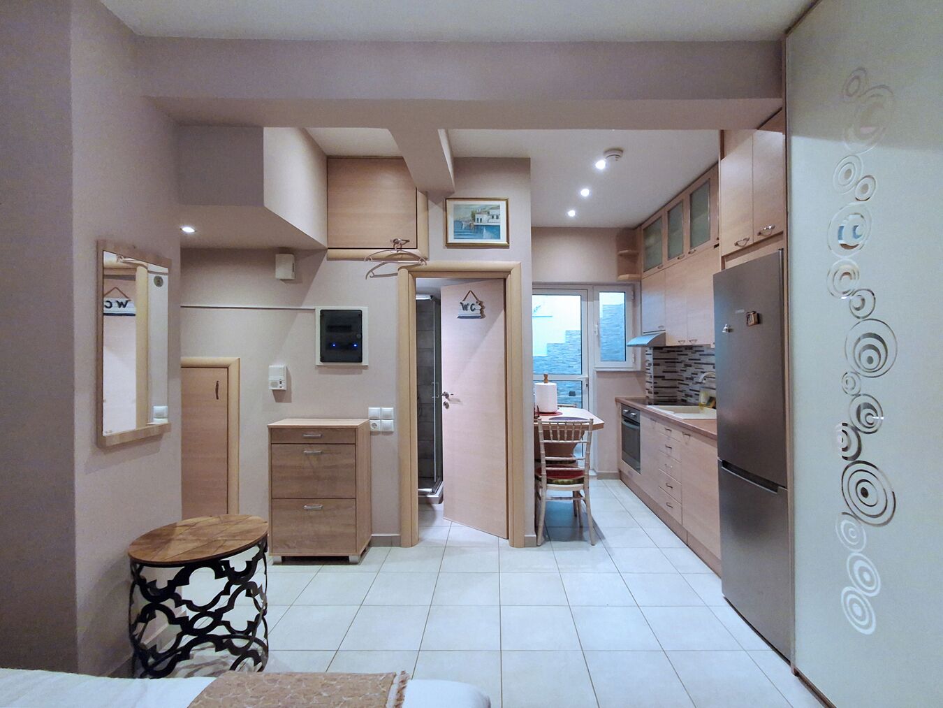 A modern kitchen with a refrigerator, cabinets, and a dining area with a chair and table.
