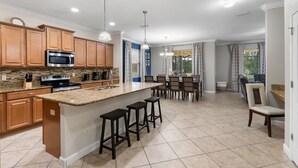 A modern kitchen with granite countertops, stainless steel appliances, wooden cabinets, and a central island with bar stools. - Buc2999 6 Bedroom Home (Kissimmee)