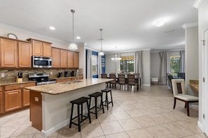 Una cocina moderna con encimeras de granito, electrodomésticos de acero inoxidable, armarios de madera y una isla central con taburetes de bar.