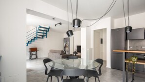 Una cocina moderna con refrigerador empotrado, un comedor con mesa y sillas de vidrio, y una escalera con barandillas azules.