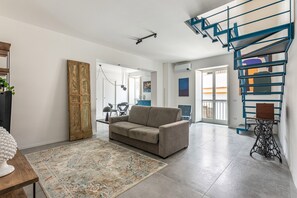 A modern living room with a sofa, a patterned rug, a vintage sewing machine, and a blue spiral staircase. - Ballar Duplex With Terrace by Wonderful Italy (Palermo)