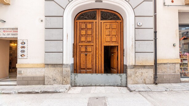 Puerta doble de madera con un arco blanco, una pequeña señal encima de la puerta, y el número '6' en la pared a la derecha.