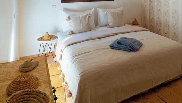 A bedroom with a bed, a window with blinds, a hanging light fixture, and a patterned wall.