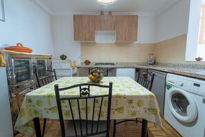 A compact kitchen with a table, chairs, a washing machine, and a microwave.