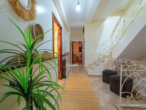 A hallway with a staircase, a woven mat, and a potted plant. - Roots Surf House (Agadir)