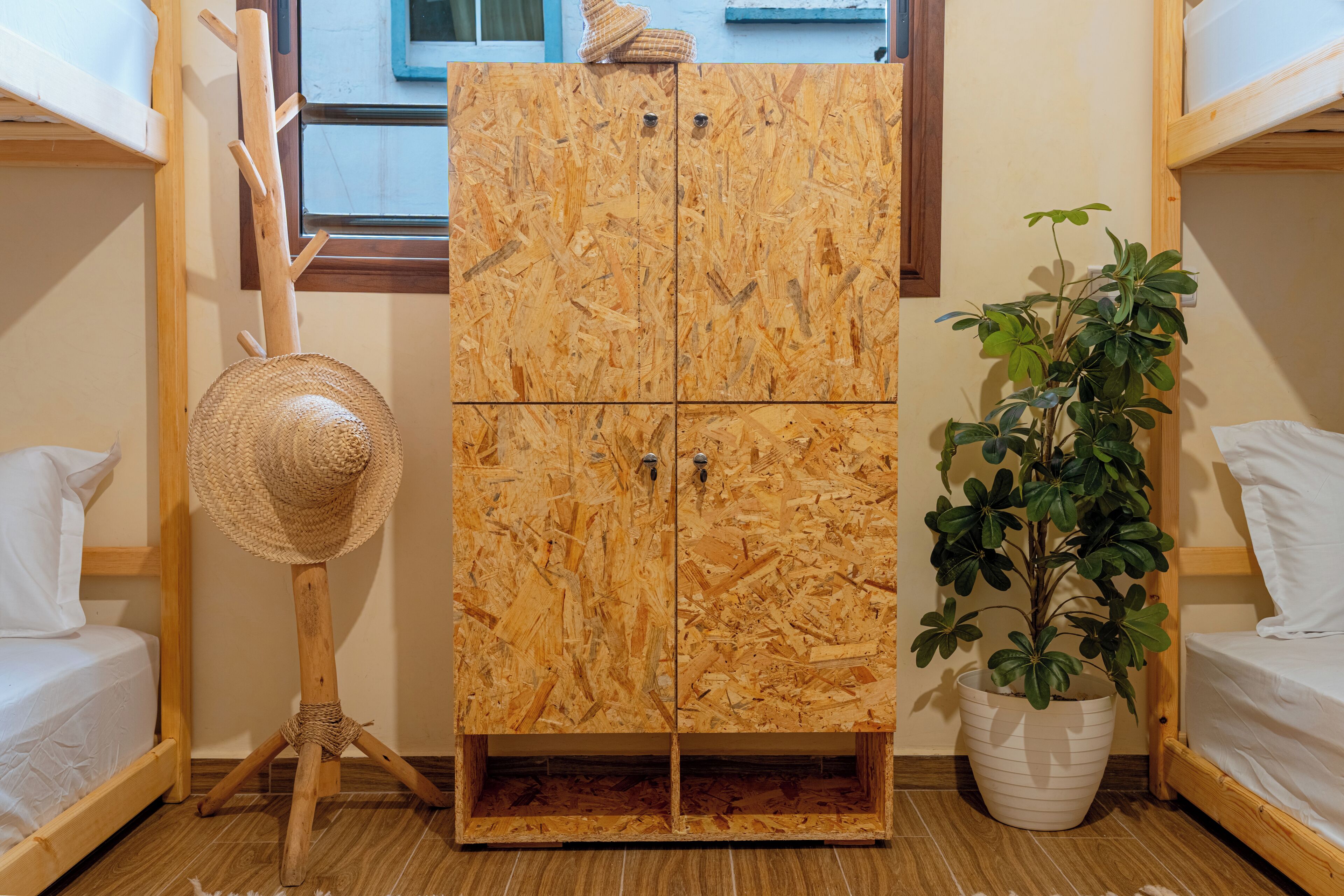 A room with a wooden cabinet, a woven hat on a stand, a potted plant, and two bunk beds.